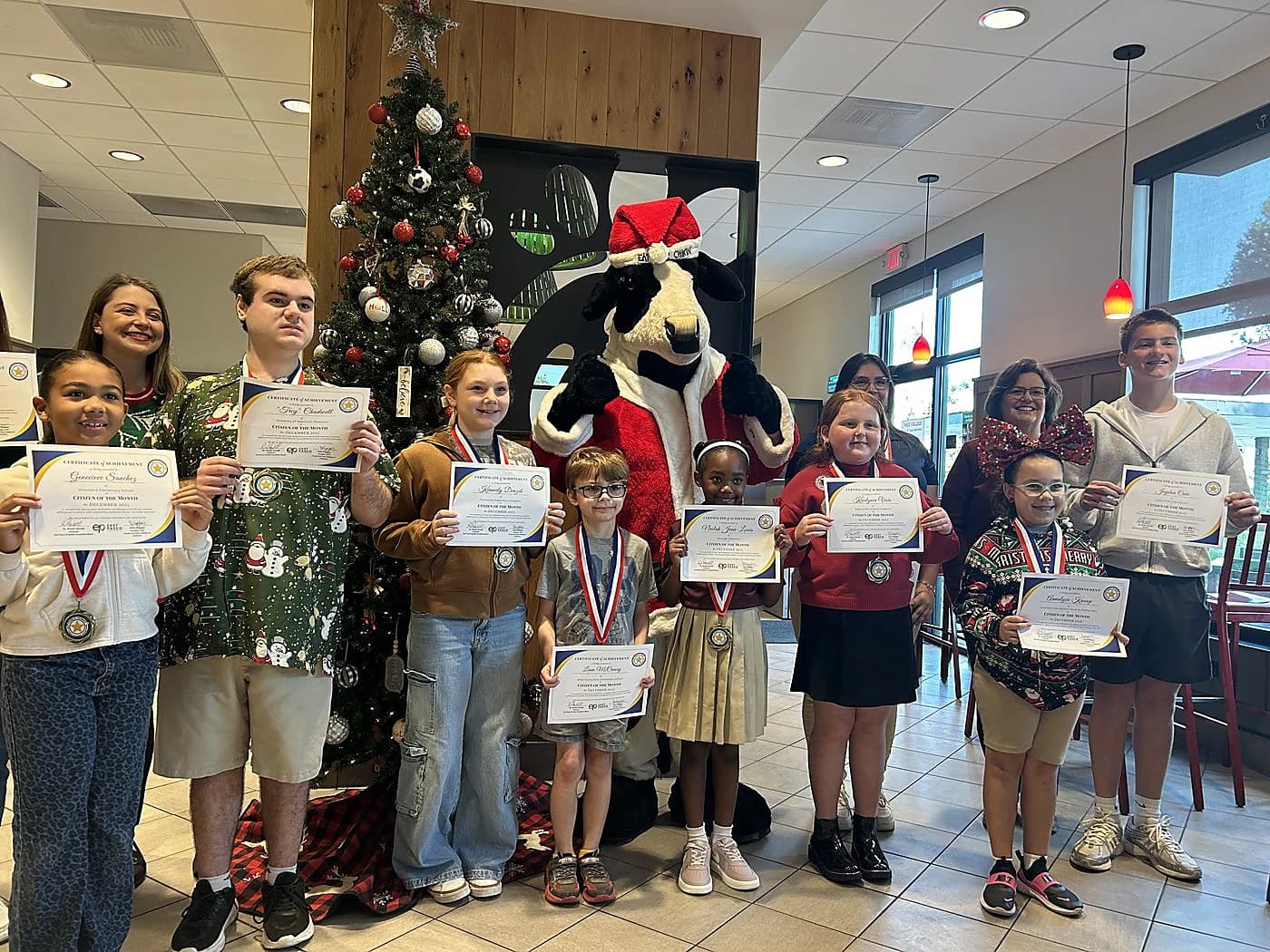 Student Citizen of the Month recipients holding certificates by the Christmas tree